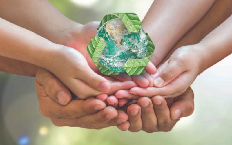 A bunch of different hands holding a green recycling symbol indicating the need of the society as one in achieving a zero waste society.